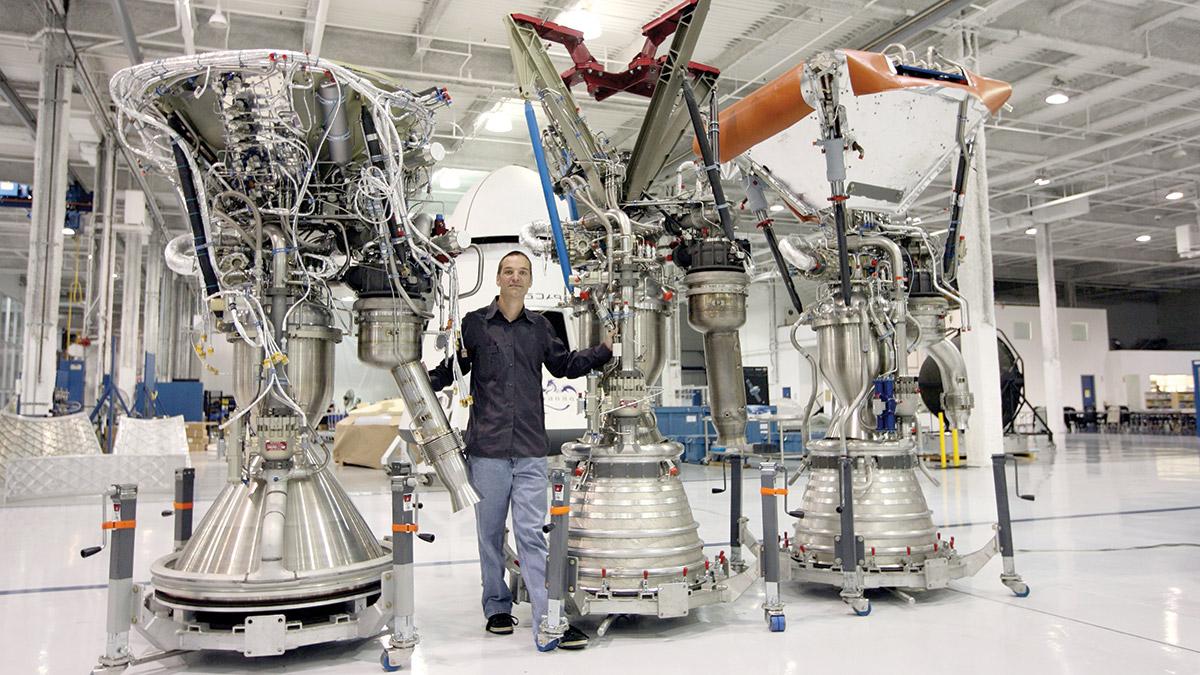Tom Mueller poses with three rocket engines, which are nearly twice as tall as he is.